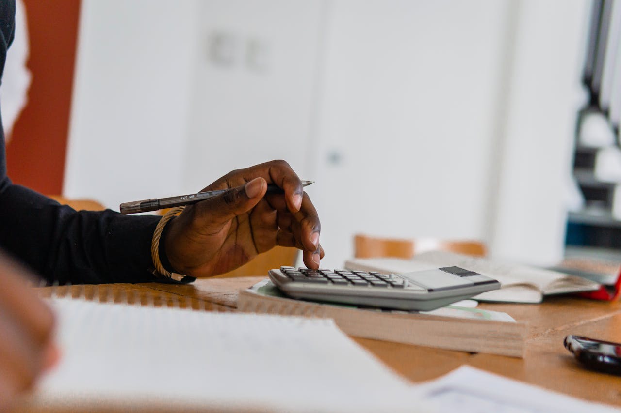 Close-up of a person using a calculator and pen for financial work at a desk.